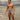 Man in a blue swimsuit standing in shallow water with a cloudy sky and distant landscape.