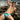 Man in blue swim trunks posing on a rocky beach with ocean waves in the background