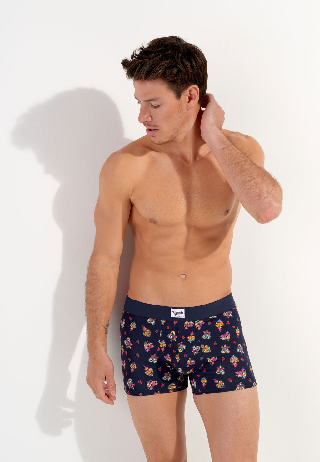 male model wearing a pair of navy blue boxer briefs with a multicolored heart pattern and a wide red elastic waistband.