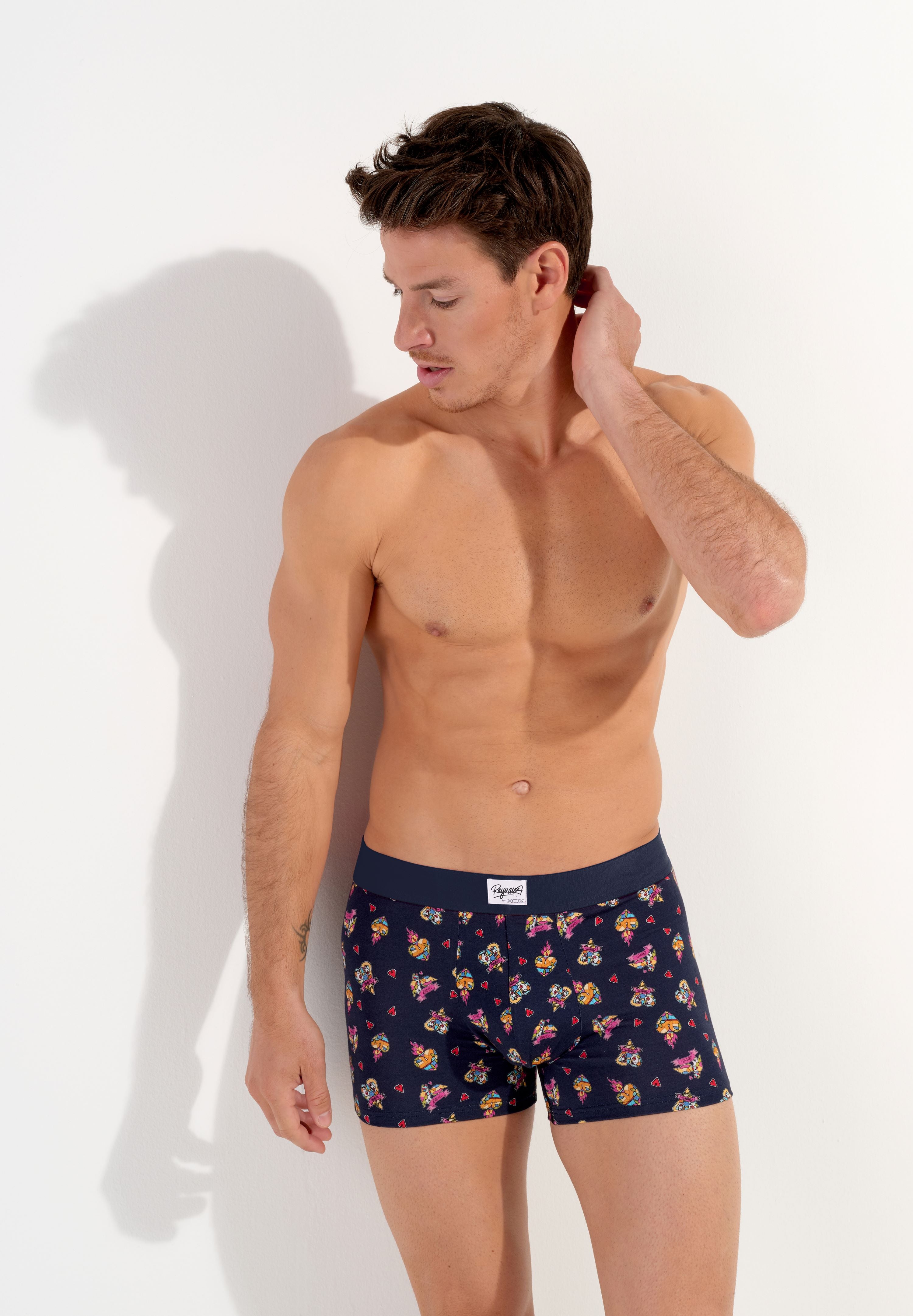 male model wearing a pair of navy blue boxer briefs with a multicolored heart pattern and a wide red elastic waistband.