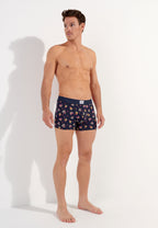 male model wearing a pair of navy blue boxer briefs with a multicolored heart pattern and a wide red elastic waistband.