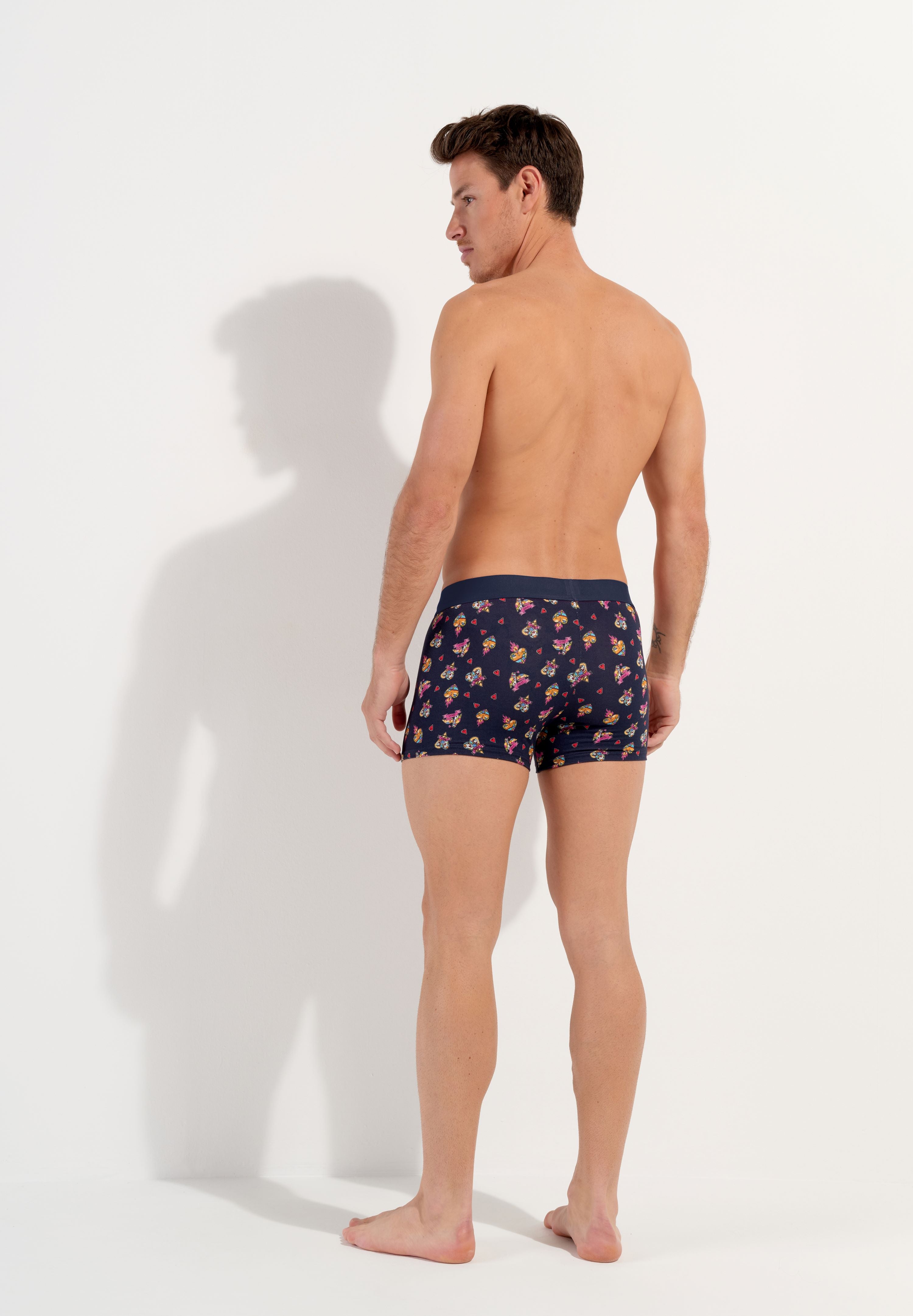 male model wearing a pair of navy blue boxer briefs with a multicolored heart pattern and a wide red elastic waistband.