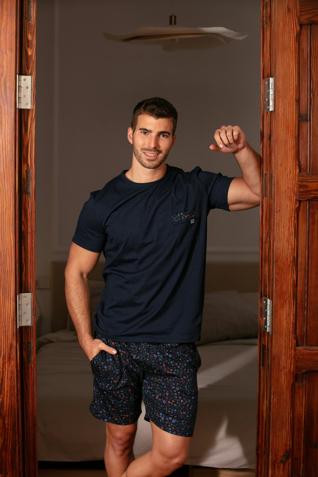 Man in navy t-shirt and patterned shorts standing in a doorway.