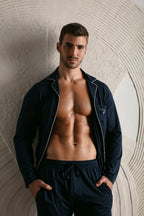 Man wearing a navy pajama set against a textured wall