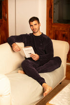 Man sitting on a couch reading a book in a cozy room.