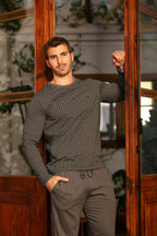 Man wearing a patterned long sleeve top and gray pants standing indoors with wooden doors.