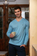 Man wearing a blue long-sleeve shirt holding a mug indoors and also navy pants