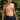 A shirtless man wearing black boxer briefs, standing outdoors against a background of green foliage.