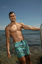 Man wearing blue swim trunks with a pattern standing on a beach.