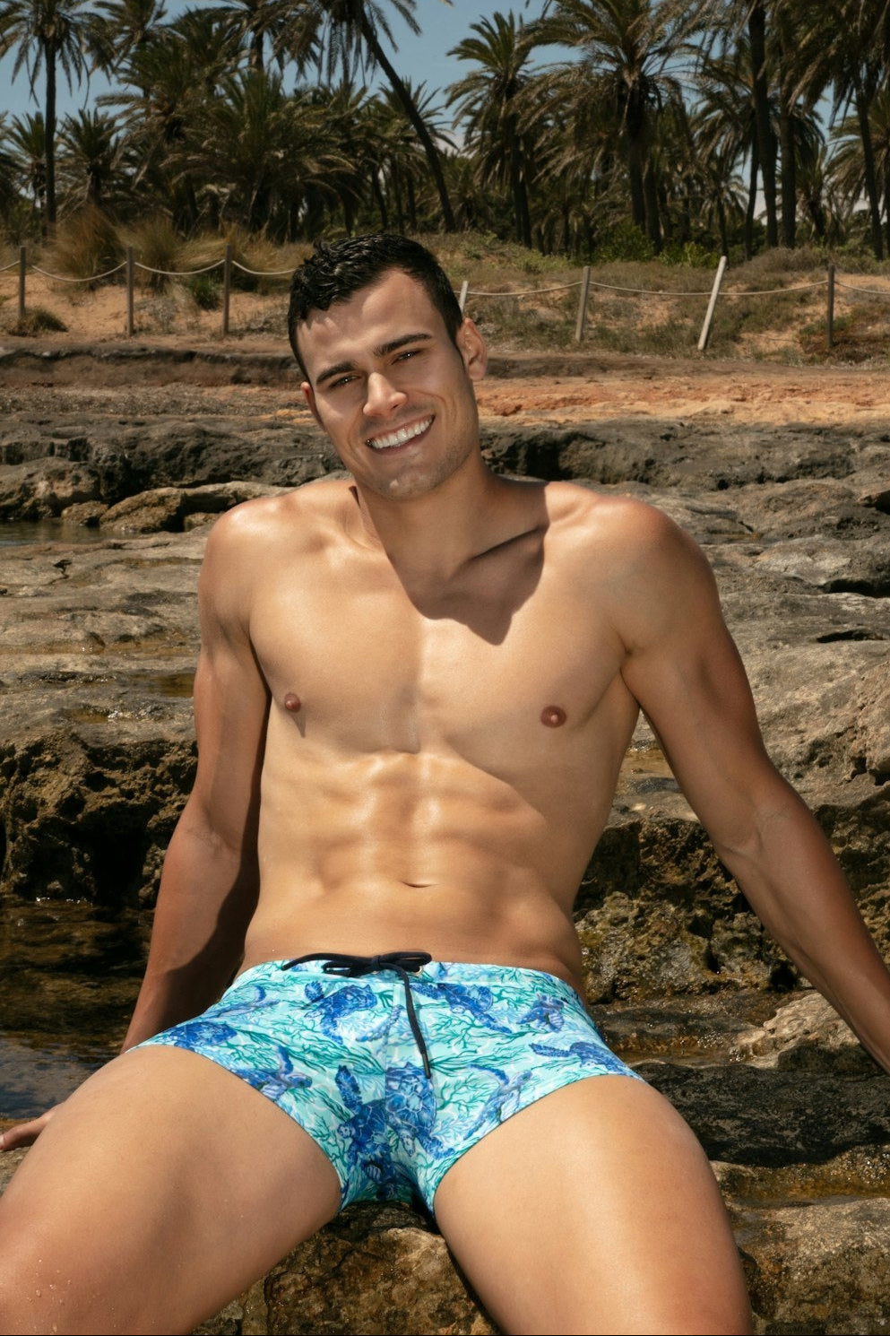 Man wearing blue swim trunks with a tropical background