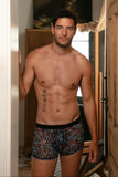 Man wearing patterned underwear standing in a room with a painting on the wall.