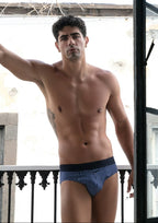 Man standing shirtless on a balcony wearing patterned underwear.