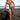 Man in blue swim trunks standing on a beach with a kite in the background