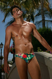 Man wearing a colorful swimsuit with palm trees and a building in the background