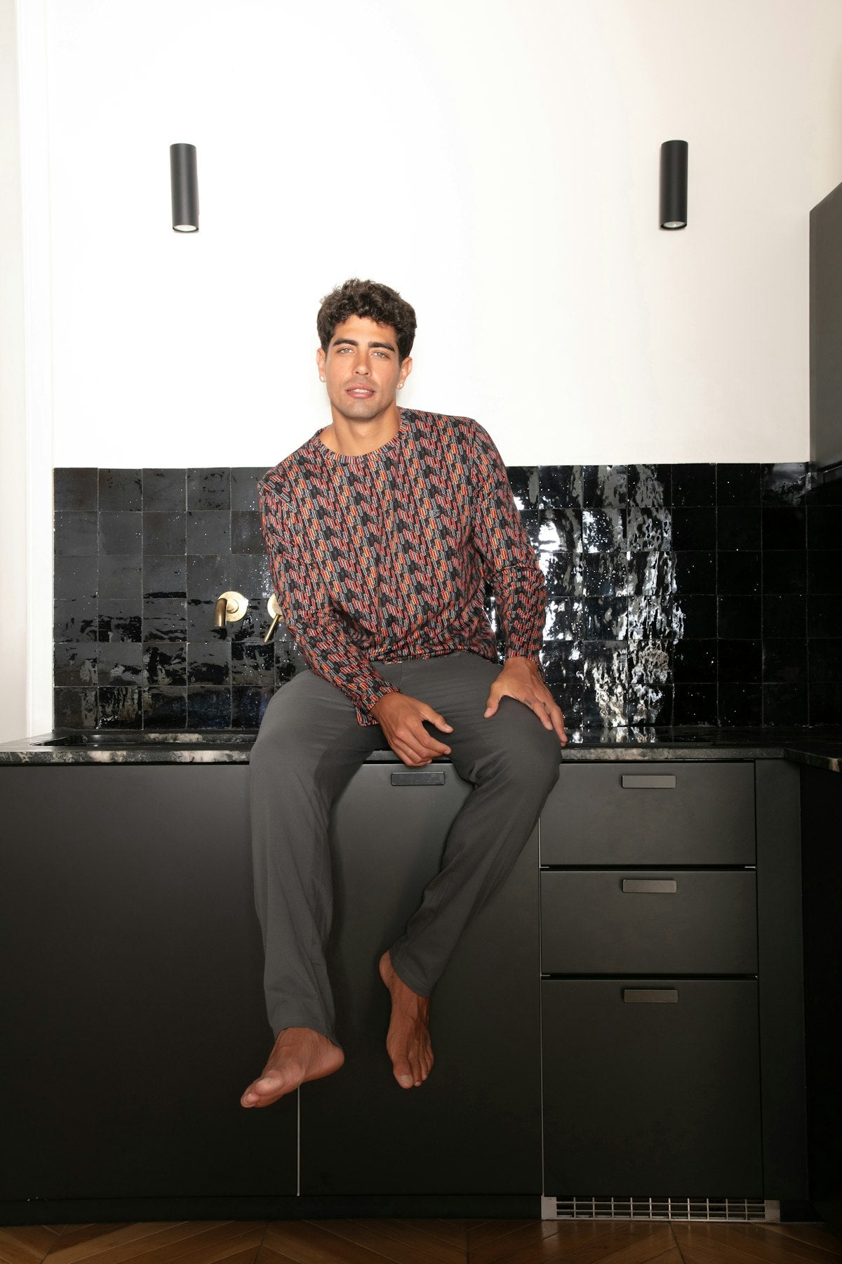 Man sitting on a black kitchen counter with a modern backsplash.