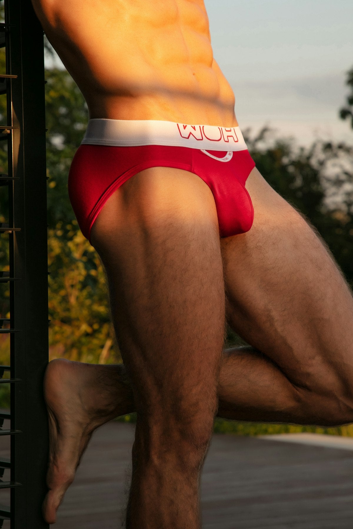 Person wearing red briefs with a logo, standing outdoors.