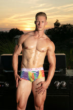 Man wearing colorful underwear with 'WOH' brand logo outdoors at sunset.