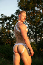 Person wearing a white harness and jock strap outdoors with trees in the background